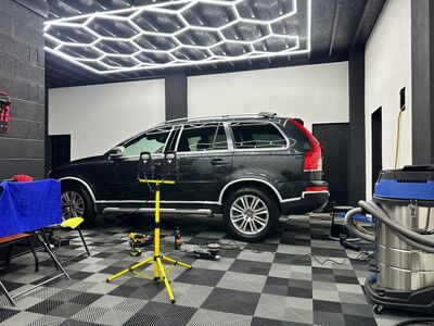 Black Volvo XC90 SUV under work lights during ceramic coating application